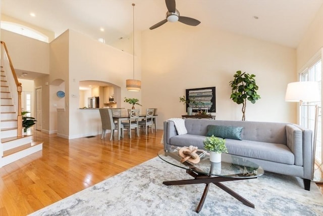 living room with light wood-style flooring, stairway, arched walkways, baseboards, and ceiling fan