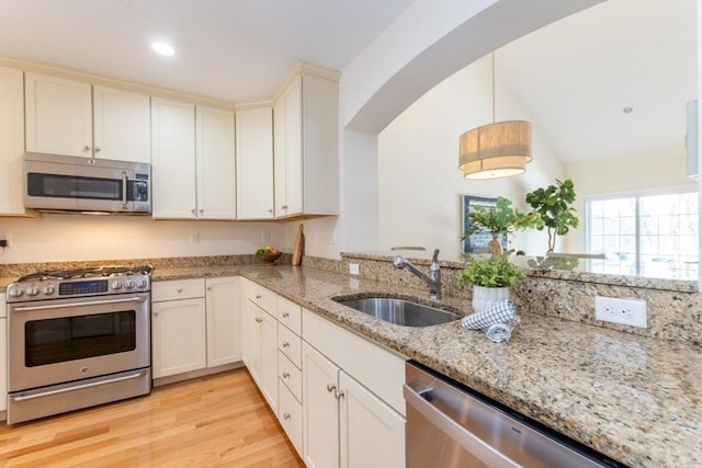 kitchen featuring light stone countertops, light wood-style flooring, hanging light fixtures, stainless steel appliances, and a sink