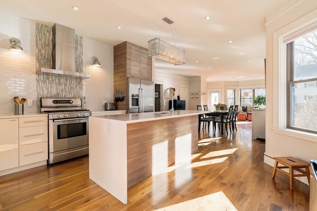 kitchen with stainless steel appliances, light countertops, wall chimney range hood, and modern cabinets