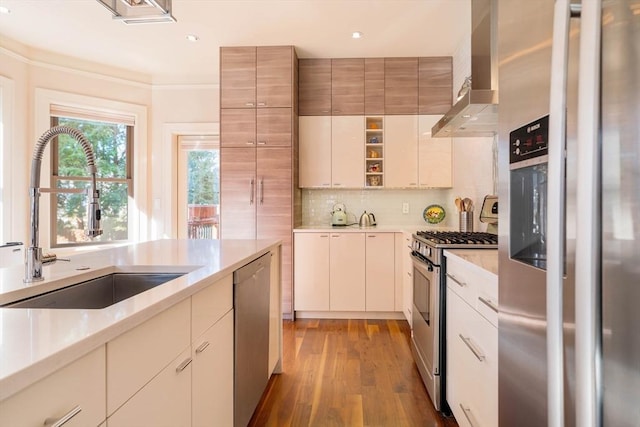 kitchen with tasteful backsplash, wall chimney range hood, light countertops, appliances with stainless steel finishes, and a sink