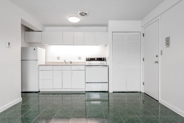 kitchen with freestanding refrigerator, range, baseboards, white cabinetry, and dark tile patterned flooring