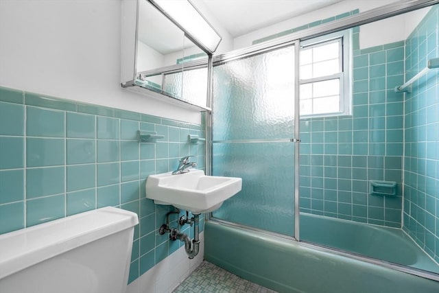 bathroom featuring combined bath / shower with glass door, toilet, tile walls, tile patterned floors, and a sink