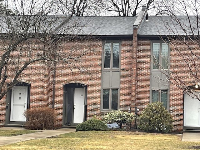 view of front of home with brick siding, a front yard, and a shingled roof