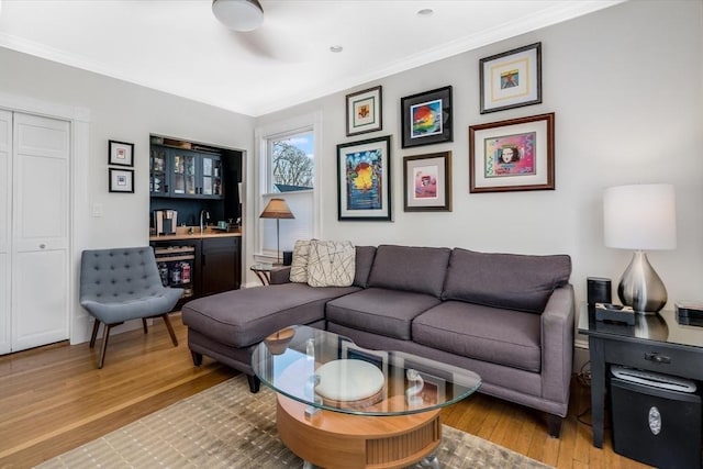 living room with light hardwood / wood-style floors, crown molding, and indoor bar