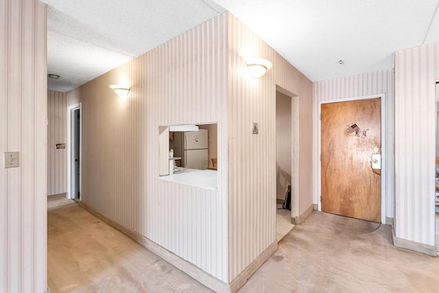 hallway featuring a textured ceiling, wallpapered walls, and baseboards