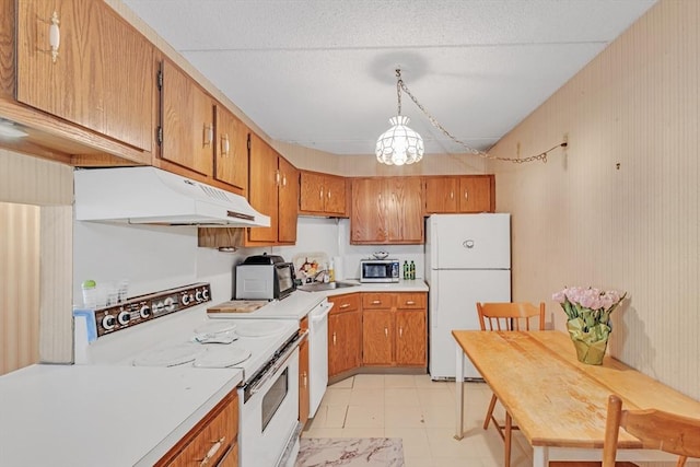 kitchen with white appliances, brown cabinetry, under cabinet range hood, and a sink