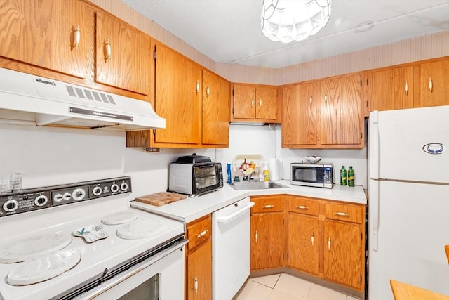 kitchen with brown cabinets, under cabinet range hood, a sink, white appliances, and light countertops