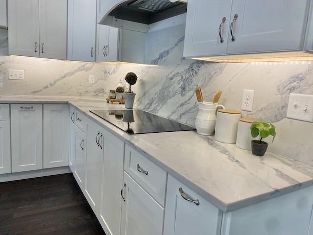 kitchen featuring light stone counters, dark wood-type flooring, black electric cooktop, under cabinet range hood, and backsplash