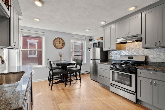 kitchen featuring appliances with stainless steel finishes, dark stone countertops, light hardwood / wood-style flooring, plenty of natural light, and gray cabinets