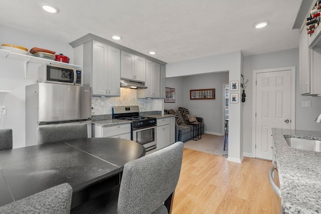 kitchen with sink, backsplash, light wood-type flooring, gray cabinetry, and stainless steel appliances