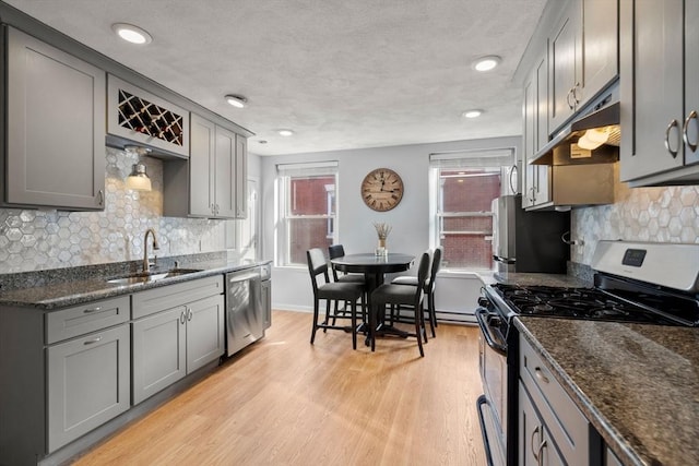 kitchen featuring sink, dark stone countertops, light hardwood / wood-style flooring, and appliances with stainless steel finishes