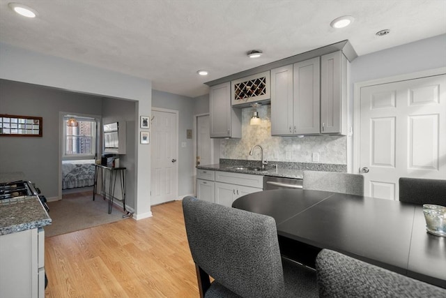 kitchen with dishwasher, sink, backsplash, gray cabinets, and light wood-type flooring