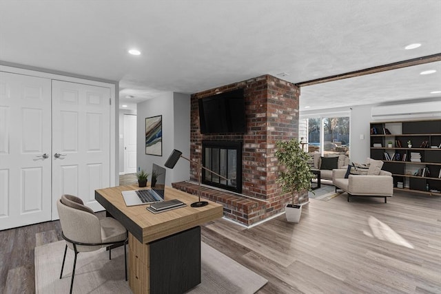 office area featuring hardwood / wood-style floors, a wall mounted air conditioner, and a brick fireplace