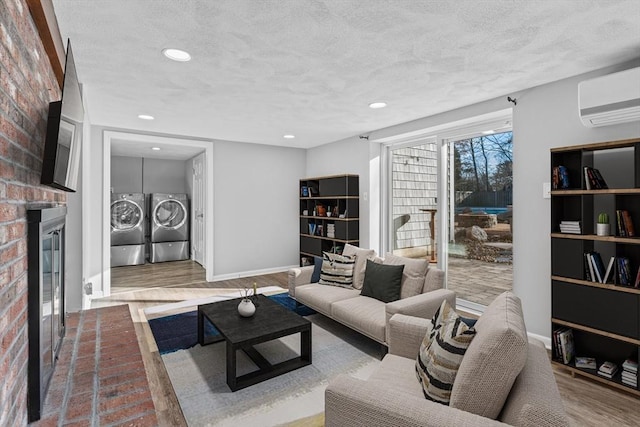 living room with a wall mounted air conditioner, a brick fireplace, separate washer and dryer, wood-type flooring, and a textured ceiling