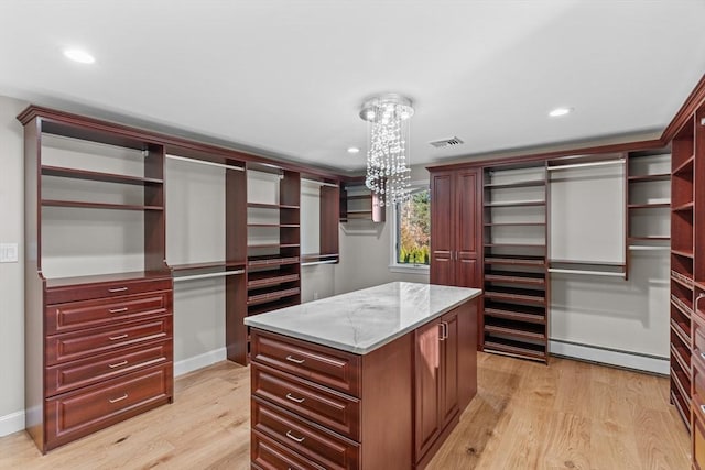 spacious closet featuring an inviting chandelier, light hardwood / wood-style floors, and a baseboard radiator