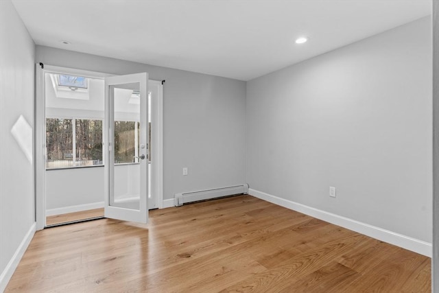 empty room featuring a skylight, light hardwood / wood-style flooring, and a baseboard radiator