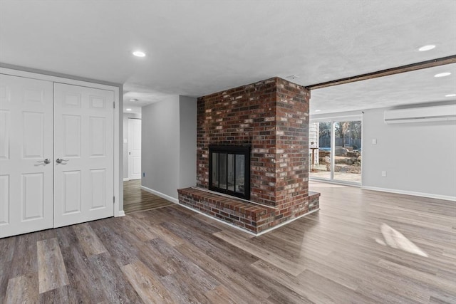 unfurnished living room featuring wood-type flooring, a brick fireplace, and an AC wall unit