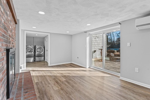 unfurnished living room featuring a brick fireplace, a textured ceiling, a wall unit AC, wood-type flooring, and independent washer and dryer