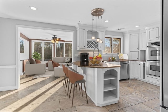 kitchen with a kitchen bar, stainless steel appliances, ceiling fan, decorative light fixtures, and white cabinets