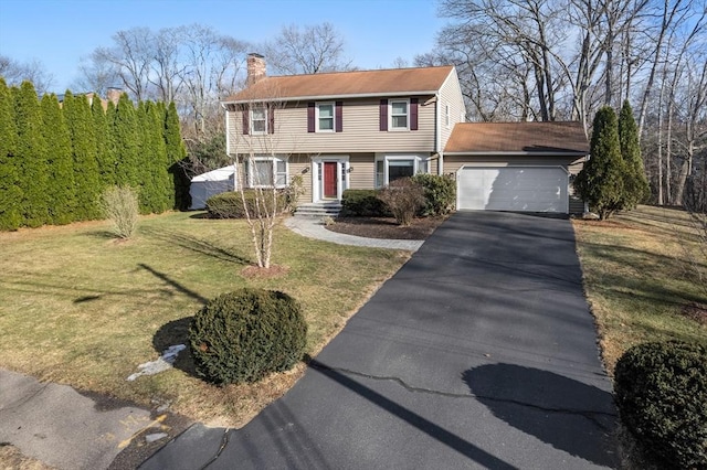 colonial home featuring aphalt driveway, an attached garage, a front yard, and a chimney