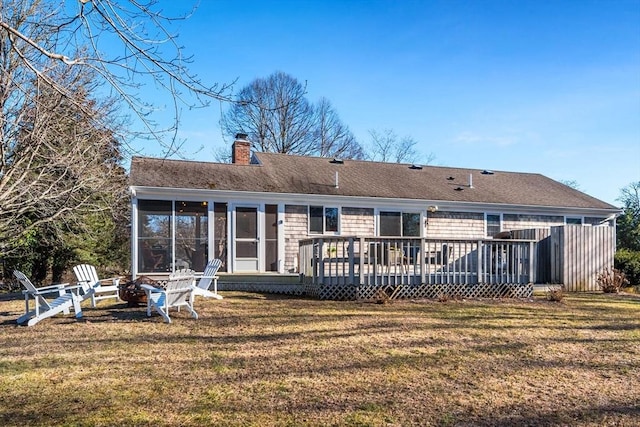 back of property with a wooden deck, an outdoor fire pit, a sunroom, and a lawn