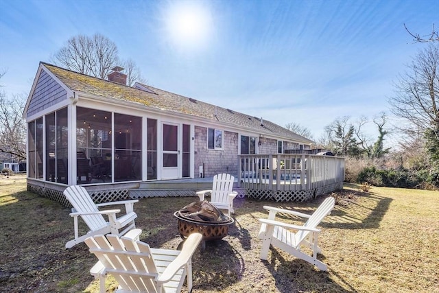 back of property featuring a sunroom, a lawn, a deck, and an outdoor fire pit