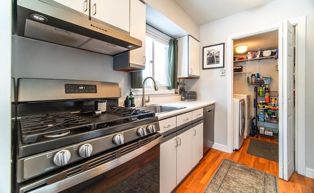 kitchen with under cabinet range hood, white cabinetry, appliances with stainless steel finishes, and independent washer and dryer