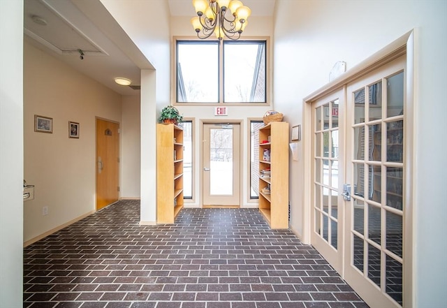 foyer entrance featuring brick floor, a high ceiling, a notable chandelier, and french doors