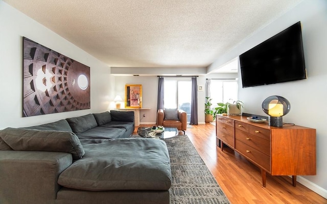 living room featuring a textured ceiling, light wood finished floors, and baseboards