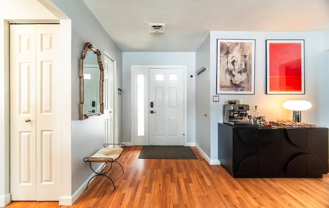 foyer entrance featuring visible vents, a textured ceiling, baseboards, and wood finished floors