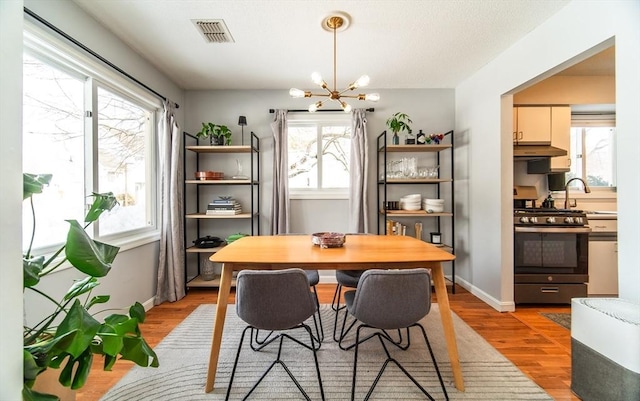 dining area with baseboards, light wood-style flooring, visible vents, and an inviting chandelier