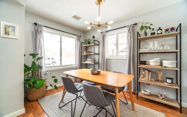 dining room with a chandelier, wood finished floors, visible vents, and baseboards