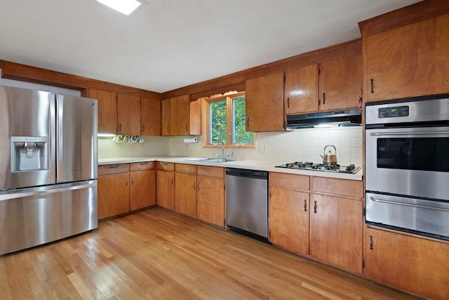 kitchen with backsplash, sink, light hardwood / wood-style floors, and appliances with stainless steel finishes