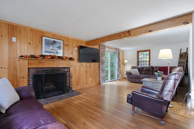 living room with beam ceiling, hardwood / wood-style flooring, a brick fireplace, and wood walls