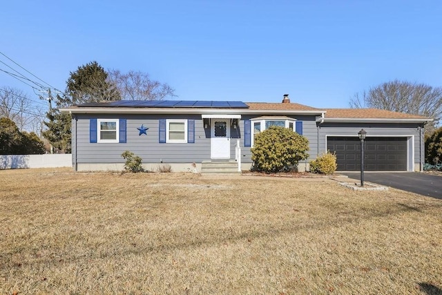 ranch-style home with aphalt driveway, an attached garage, entry steps, roof mounted solar panels, and a front lawn