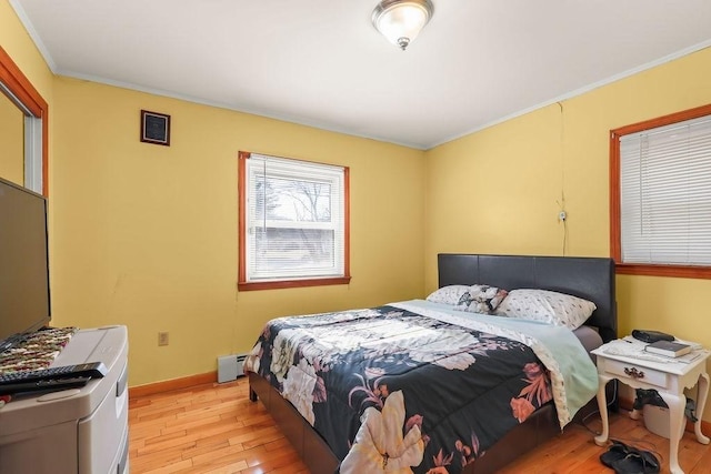 bedroom featuring a baseboard radiator, crown molding, light wood-style flooring, and baseboards