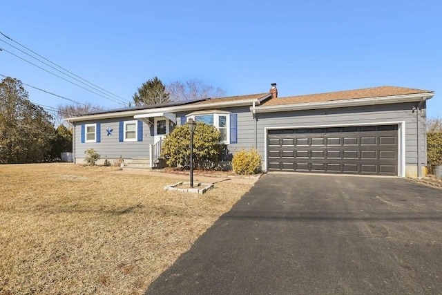 ranch-style house featuring aphalt driveway, a chimney, an attached garage, and a front lawn