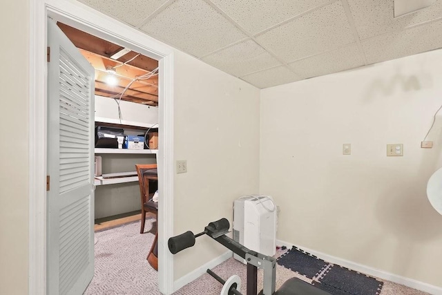 workout room featuring a paneled ceiling, light carpet, and baseboards