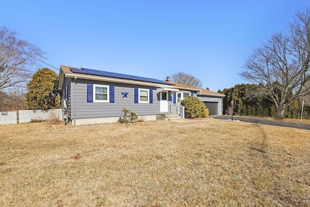 single story home with solar panels, fence, a garage, driveway, and a front lawn