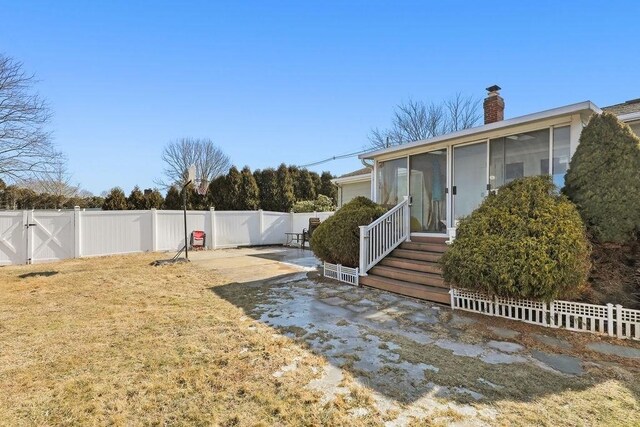 view of yard featuring a sunroom, a fenced backyard, and a gate