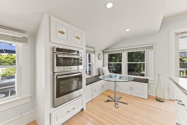 kitchen with double oven, white cabinetry, light wood-type flooring, healthy amount of natural light, and lofted ceiling