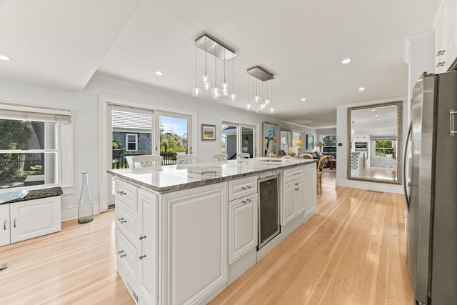 kitchen featuring freestanding refrigerator, beverage cooler, white cabinets, hanging light fixtures, and light wood-style floors