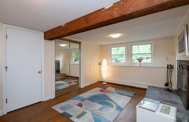 46 Plum St, Hamilton, MA 01982 - living area with baseboard heating, a fireplace with raised hearth, wood finished floors, beamed ceiling, and plenty of natural light