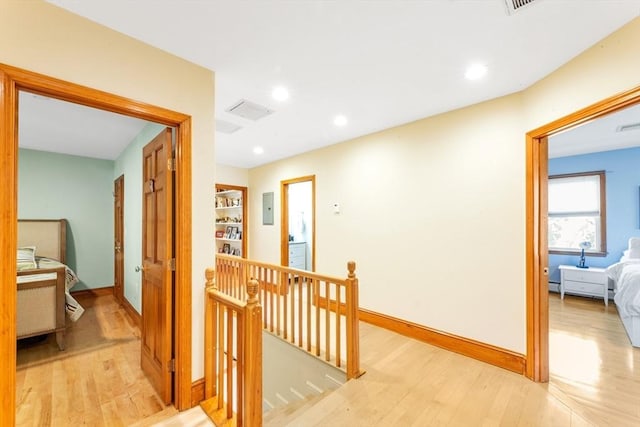 hallway featuring an upstairs landing, light wood-style floors, baseboards, recessed lighting, and electric panel
