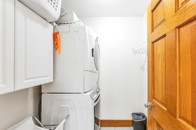 washroom featuring stacked washer and clothes dryer, cabinet space, baseboards, and tile patterned floors