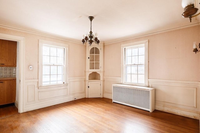 unfurnished dining area featuring ornamental molding, radiator heating unit, a chandelier, and hardwood / wood-style floors