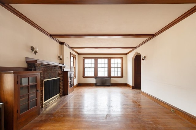 unfurnished living room featuring wood-type flooring, radiator, crown molding, and a fireplace