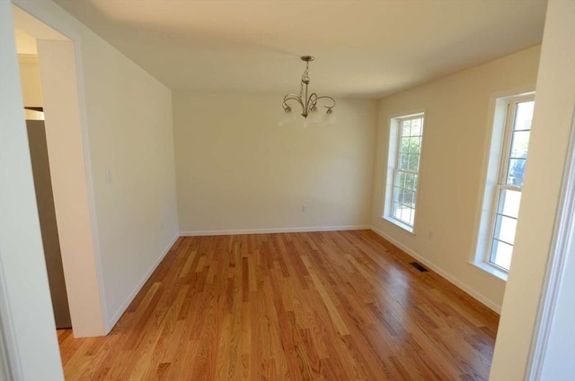 empty room with light hardwood / wood-style floors and a notable chandelier