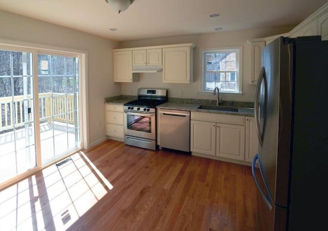 kitchen featuring sink, stone countertops, wood-type flooring, stainless steel appliances, and white cabinets