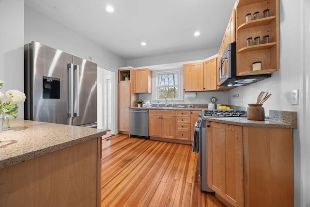 kitchen with stainless steel appliances, light stone countertops, sink, and light hardwood / wood-style flooring